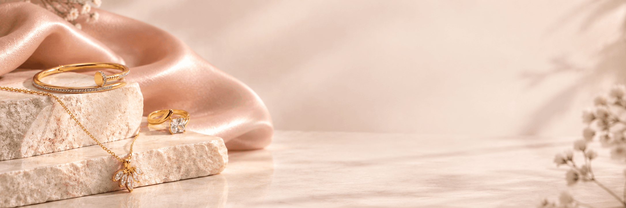 Gold jewelry arranged on blush silk and natural stone